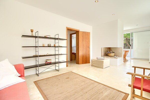 A modern living room with a red sofa, a wooden floor, a large rug, a metal shelving unit, and a kitchen area with a stone fireplace. - Rifugio sul Mare by LoveSud (Torre Vado)