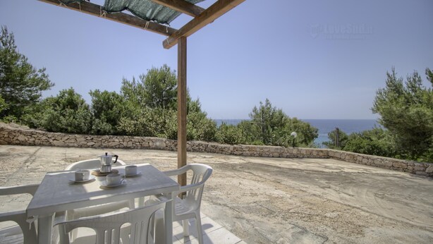 Un patio al aire libre con una mesa dispuesta para dos, con vistas panorámicas al mar y la vegetación.