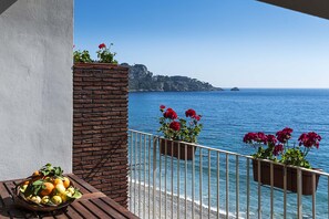 A balcony with a view of the sea, a brick wall, and a table with fruit and flowers. - Lovely seafront flat - 2 pax (Taormina)