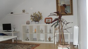 A living room with a white TV stand, a white console table with decorative items, a large potted plant, and a mirror on the wall.