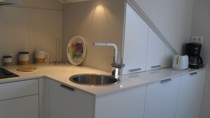 A modern kitchen with a stainless steel sink, white cabinets, and a coffee maker.