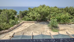 Vista di un cortile con pavimento in cemento, alberi e un muro in pietra.