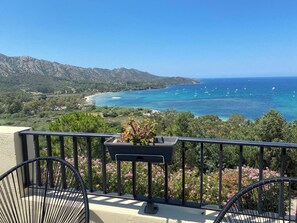 Ein Balkon mit Blick auf eine Küstenlandschaft, inklusive Strand und Booten auf dem Wasser.