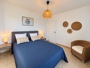A bedroom with a large bed, two bedside lamps, a door, and a wicker chair.