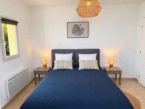 Een slaapkamer met een groot bed, twee nachtkastjes met lampen, een raam, een radiator en een kunstwerk aan de muur.