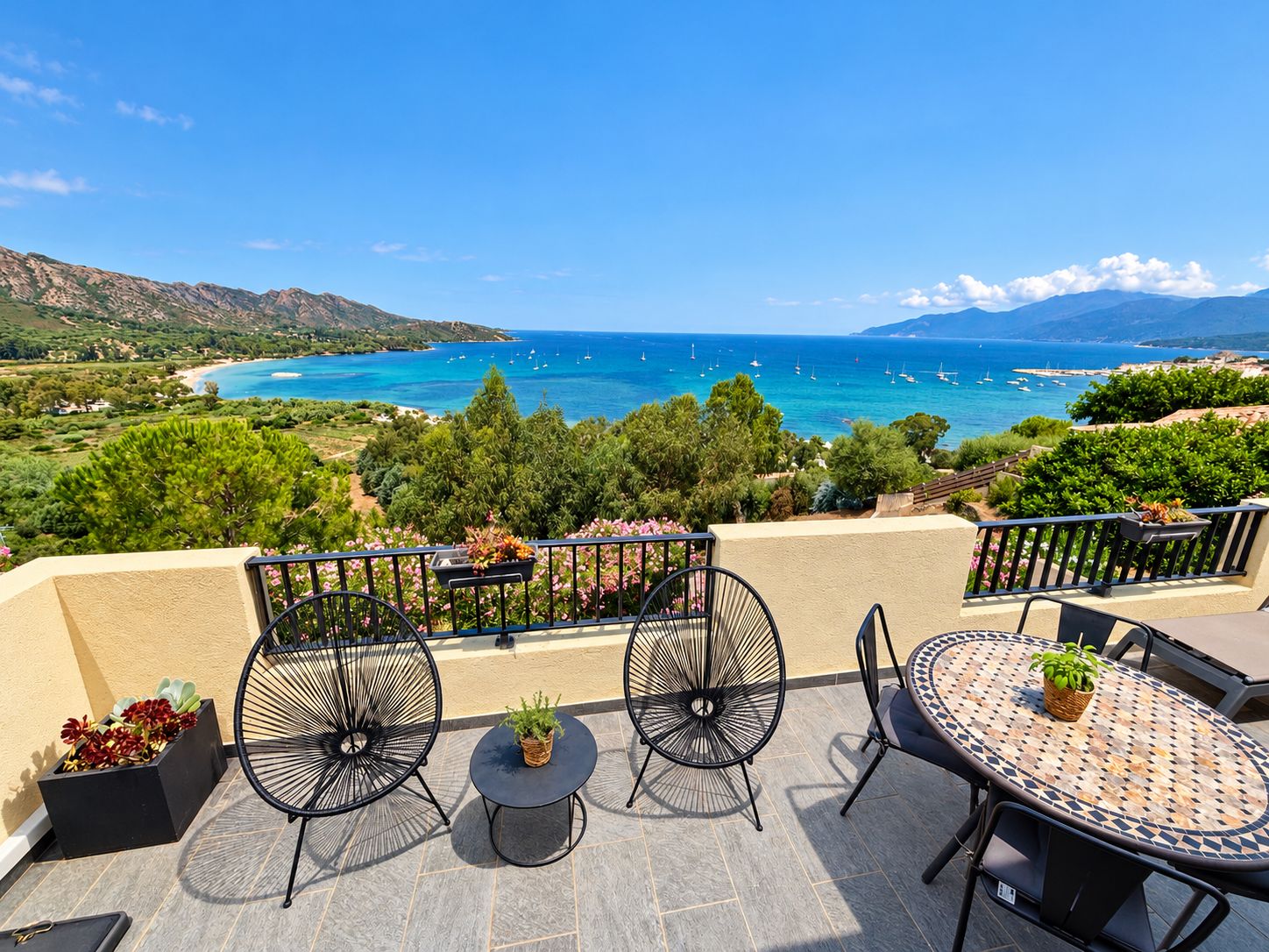 A terrace with outdoor seating, a view of the sea, and surrounding greenery.