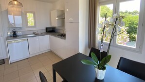 Una cocina moderna con armarios blancos, microondas y cocina a gas. Hay una mesa de comedor con sillas y una orquídea en maceta.