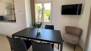 Una cocina moderna con estufa a gas, microondas y televisor montado en la pared. Hay una mesa de comedor con sillas y una planta en maceta.