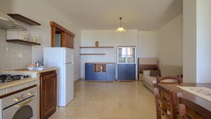 A compact kitchen with a stove, oven, and refrigerator. There is a dining area with a table and chairs. - Il Cedro San Gregorio by LoveSud (Marina San Gregorio)