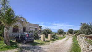 A stone building with a car parked in front, a gravel path, and a view of the sea. - Il Cedro San Gregorio by LoveSud (Marina San Gregorio)