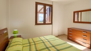 A bedroom with a bed, a dresser, a nightstand with a lamp, and a window with a view. - Il Cedro San Gregorio by LoveSud (Marina San Gregorio)