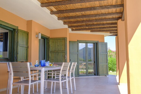 A covered patio with a table and chairs, wooden shutters, and a view of mountains.