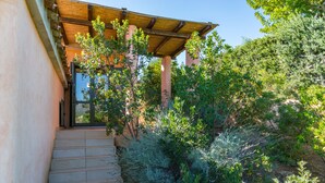 A building with a wooden pergola entrance, stone steps, and surrounding greenery. - Refined independent villa for design lovers in the beautiful Chia bay (Domus De Maria - Chia)