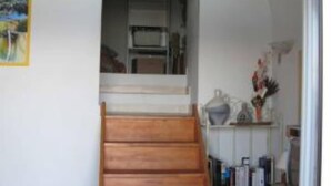 Un escalier menant à un deuxième étage, un lit avec une literie aux couleurs vives et une bibliothèque remplie de divers objets.