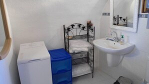 Une petite salle de bain avec un lavabo blanc, un porte-serviettes en métal avec une serviette, un lave-linge blanc et une poubelle.