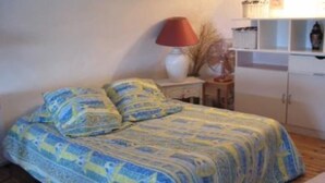 Une chambre à coucher avec un lit recouvert d’une couvre-lit à motifs, une table de chevet avec une lampe et une étagère contenant divers objets.