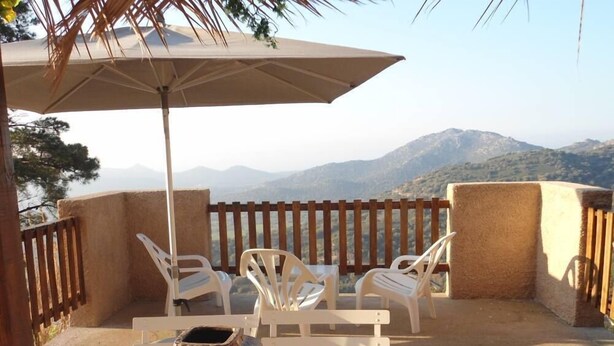 Une terrasse avec des chaises et une table en plastique blanc, un vase décoratif et un grand parasol.