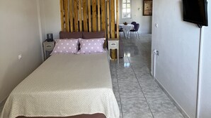 Une chambre avec un lit, une cloison en bois, un téléviseur et, au fond, un coin repas.