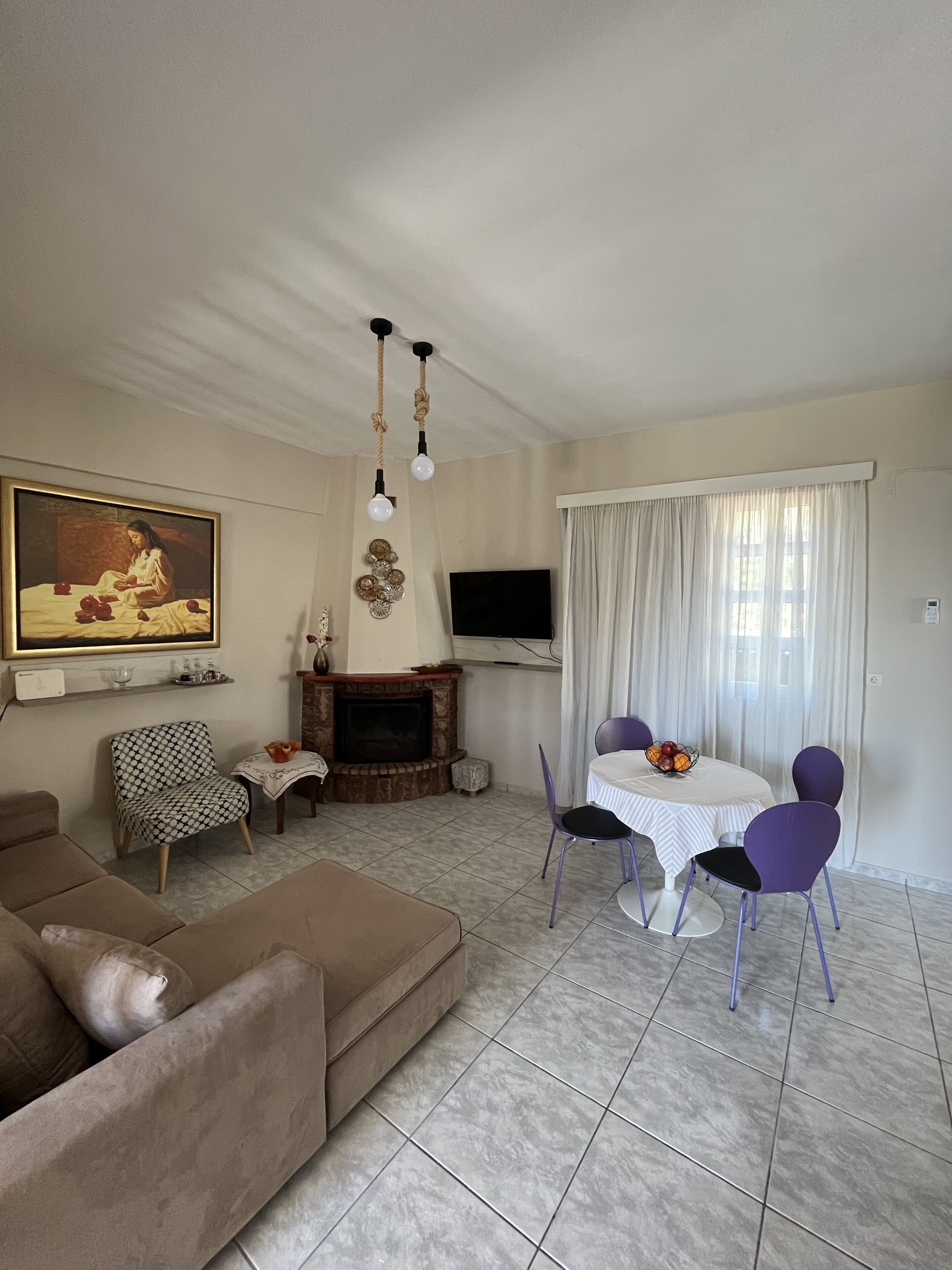 Un salon comprenant un canapé, une table à manger avec des chaises, une cheminée et un téléviseur fixé au mur.