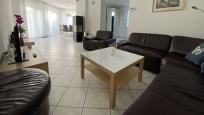 Una sala de estar moderna con un sofá, una mesa de centro y un televisor. Al fondo, un comedor con una mesa y sillas.