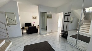 Un salón amplio con un sofá negro, un televisor de pantalla plana y una escalera con barandilla de cristal.