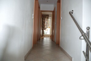 Um corredor com piso de azulejos, portas de madeira e corrimão de metal.