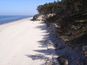 A beach with a sandy shore and a forested cliff. - Just 50 meters to the beach! Luxury vacation home in Pobierowo with a fireplace, garage, and dog (Pobierowo)
