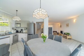 A modern kitchen with a dining area, a refrigerator, and a staircase leading to an upper level.