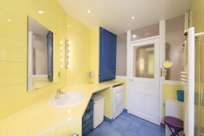 Une salle de bain avec des murs jaunes, un lavabo blanc, un miroir et une porte en verre dépoli.