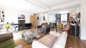 Een ruime woonkamer met een piano, banken, een salontafel en een televisie.