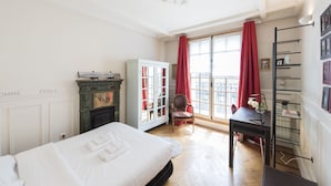 Een slaapkamer met een bed, een kledingkast, een bureau en een raam met rode gordijnen.