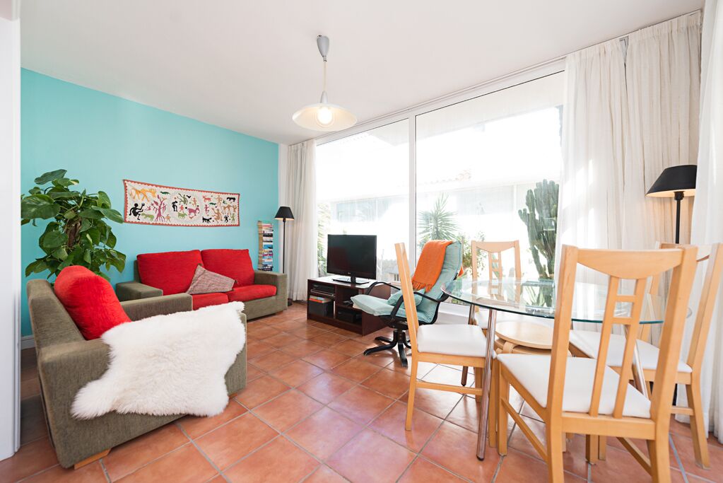 Una sala de estar con un sofá rojo, una mesa de comedor de vidrio y un televisor.