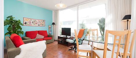 Una sala de estar con un sofá rojo, una mesa de comedor de vidrio y un televisor.