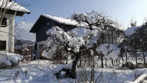 Paisagem coberta de neve com uma casa, uma cerca de madeira e céu claro.