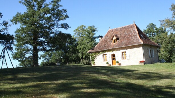 A stone house with a tiled roof, surrounded by a grassy lawn and trees.