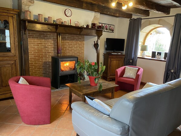 Una sala de estar acogedora con chimenea de ladrillo, muebles rojos y grises, y un televisor.