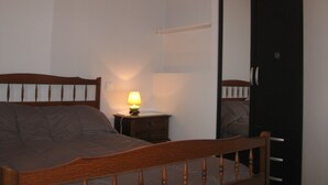 Un dormitorio con una cama de madera, una mesita de noche con lámpara y una puerta.