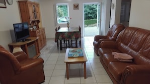 Una sala de estar con un sofá de cuero marrón, una mesa de centro de madera, un televisor sobre un mueble bajo y una mesa de comedor con sillas.