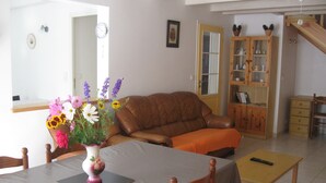 Een woonkamer met een bruine leren bank, een eettafel met stoelen, een houten kast en een vaas met bloemen.