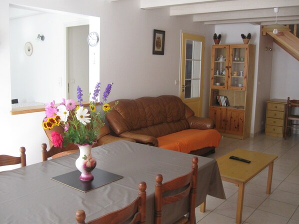 A living room with a brown leather sofa, a dining table with chairs, a wooden cabinet, and a vase with flowers.