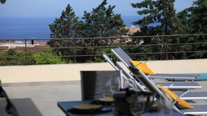 An outdoor dining area with tables and chairs, overlooking a scenic view of the ocean and trees. - Contemporary villa, with clim-160 m2, swimming pool, 5 mn from beaches & shops (Monticello)