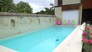A swimming pool with a stone wall and a small arched window. There are colorful chairs and a dog near the pool. - In the heart of Fontevraud-l'Abbaye (Fontevraud-L'abbaye)