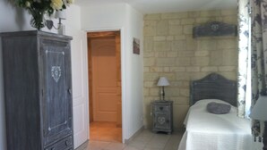 A bedroom with a bed, a dresser, a nightstand, a lamp, and a stone wall. - In the heart of Fontevraud-l'Abbaye (Fontevraud-L'abbaye)