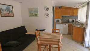 A compact living space with a dark-colored sofa, a small dining table with chairs, a kitchen area with wooden cabinets, a microwave, and a dishwasher.