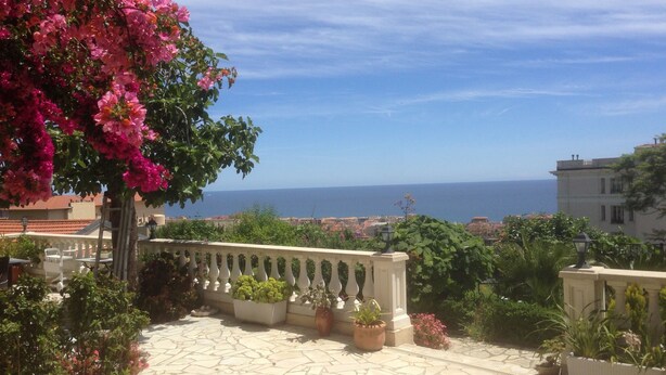 A stone-paved terrace with potted plants and a view of the sea.
