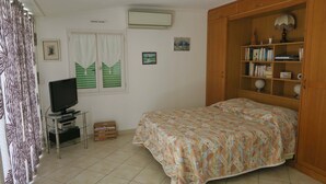 A bedroom with a bed, a television on a stand, a wooden wardrobe, and a window with shutters.