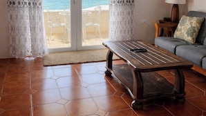A room with a wooden coffee table, a sofa, and a view of the sea through a glass door.