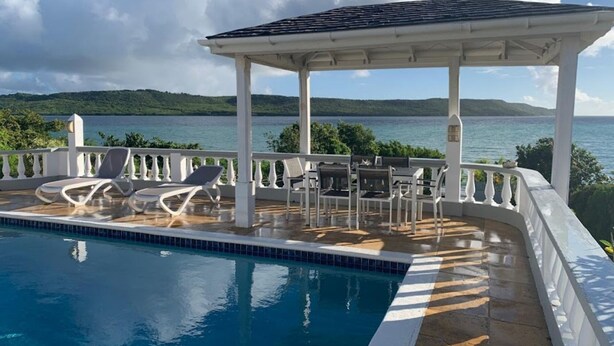 A pool area with lounge chairs and a gazebo overlooking a body of water.