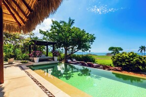 Ein Pool mit Liegestühlen, eine Pergola mit Blumen und Blick aufs Meer.