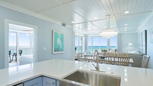 A modern kitchen with a large island, a dining area with a view, and a ceiling with exposed beams. - The Crescent 201 Beachfront Condo w/ Free Beach Service (Miramar Beach)